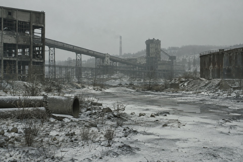 Cold abandoned industrial infrastructure with grey ash across the wintry ground.